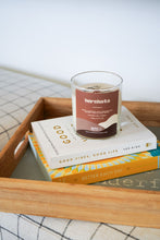 Load image into Gallery viewer, Candle with a label on top of books on a wooden tray

